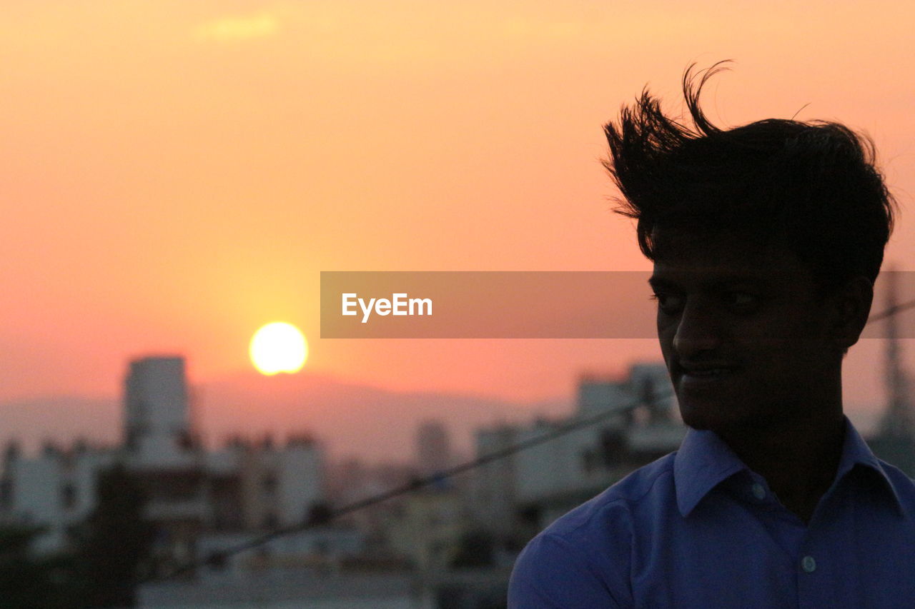 Silhouette young man looking away while standing against sky during sunset