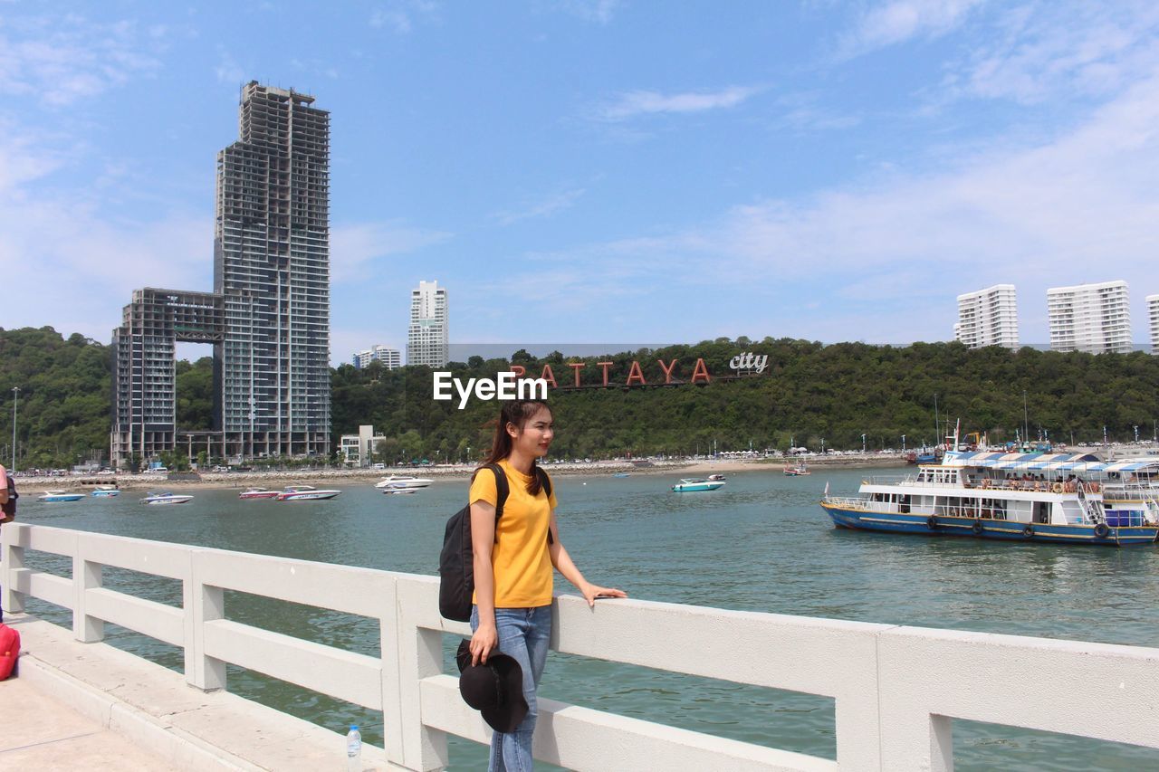 Full length of woman standing by railing against buildings in city