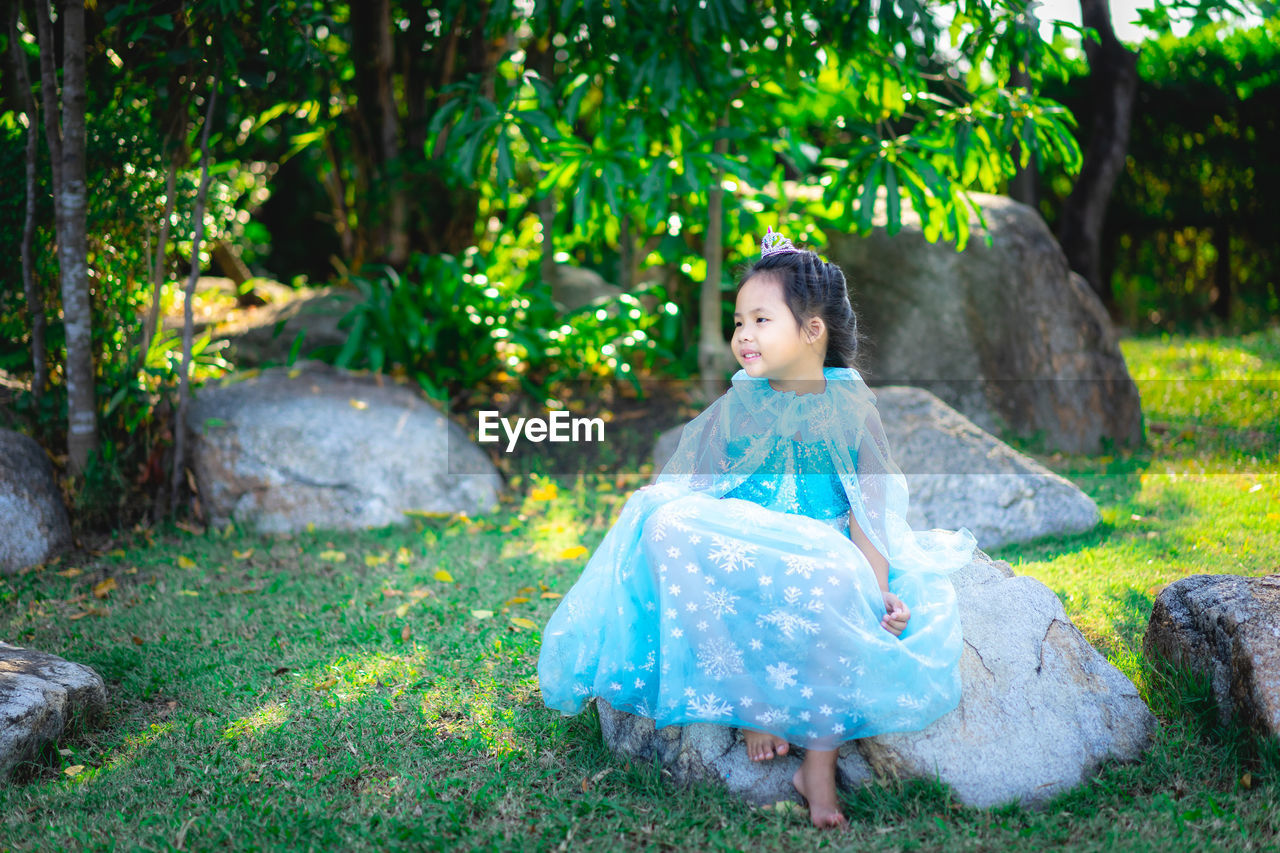 Full length of cute girl wearing dress sitting on rock in park