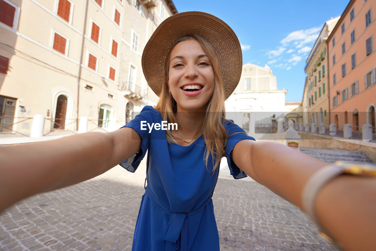 Smiling girl in blue dress and hat takes selfie picture in ancona, marche, italy