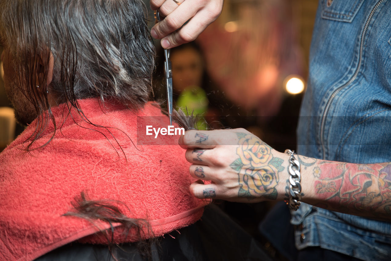 Midsection of barber with tattoos on hand cutting hair 