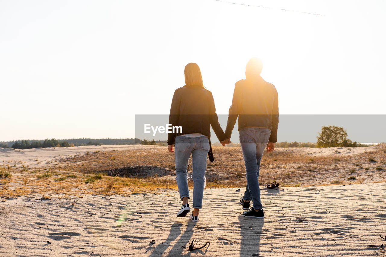 Rear view of couple holding hands while walking on land against clear sky