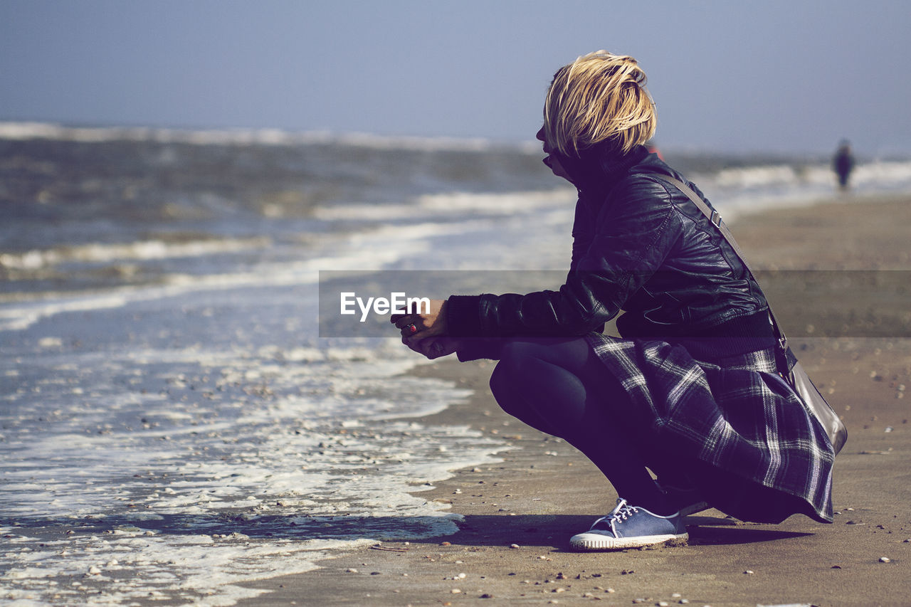 Side view full length of woman crouching on shore at beach