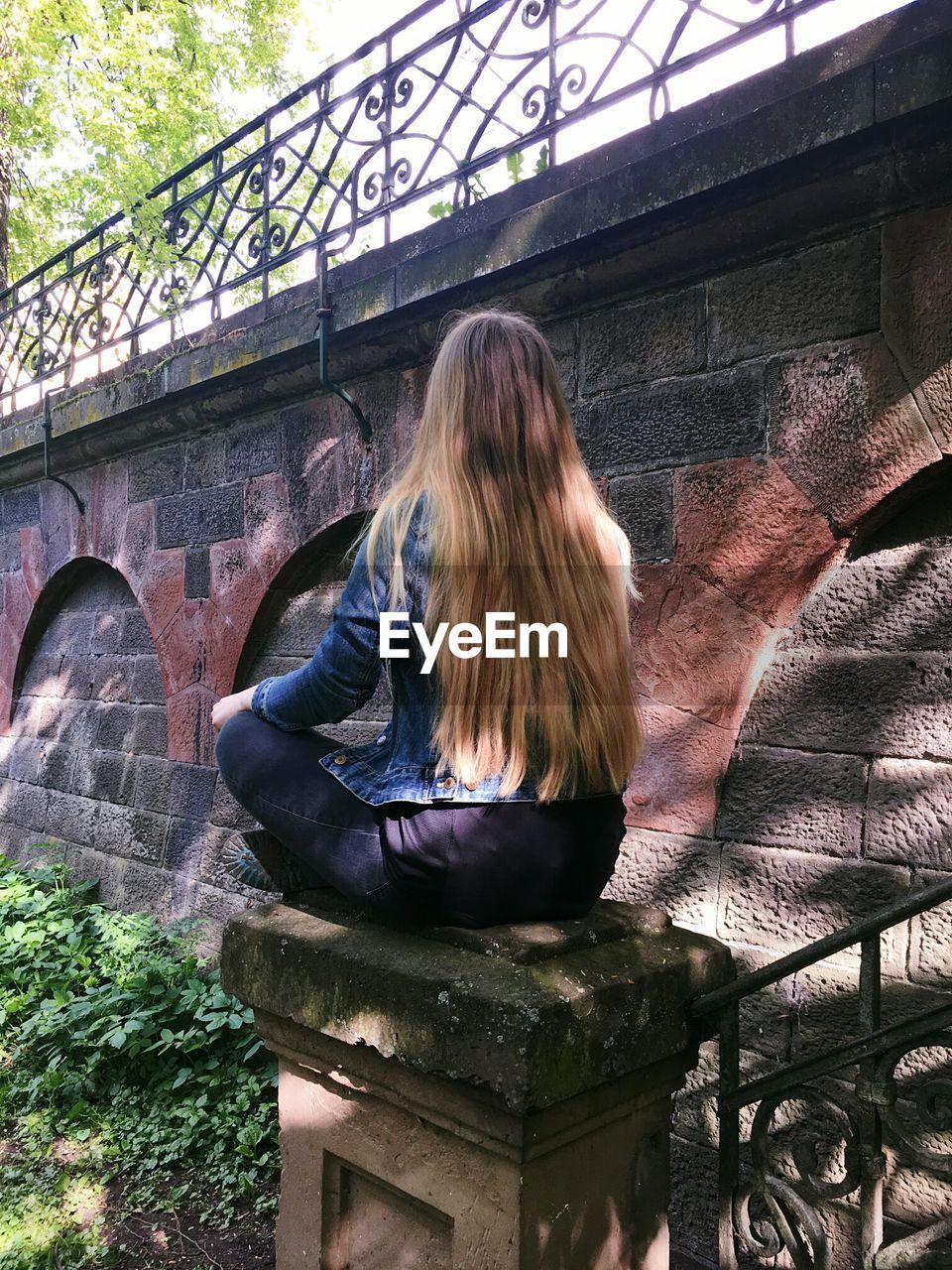 REAR VIEW OF WOMAN SITTING AGAINST BRIDGE