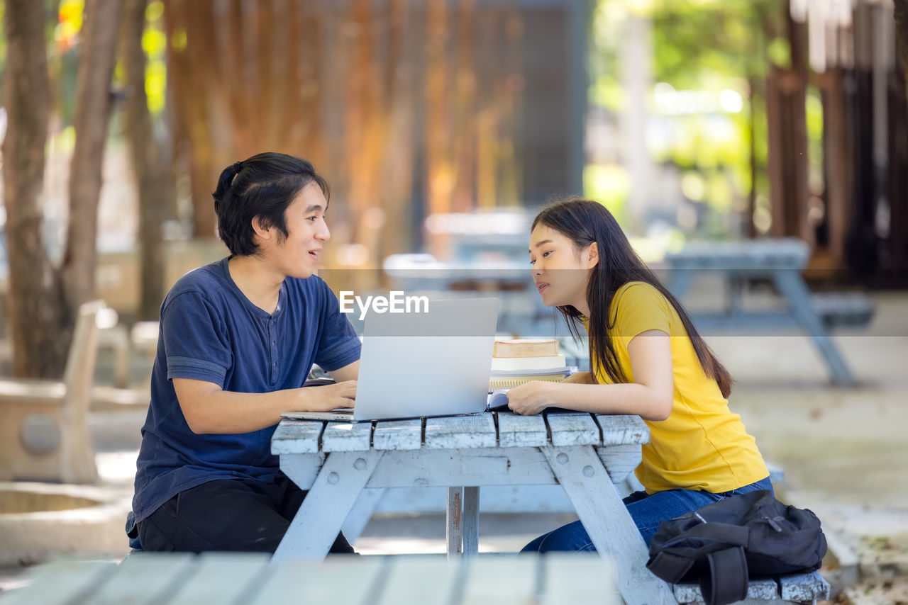 At the public park, a happy young couple using a laptop sits at a table.