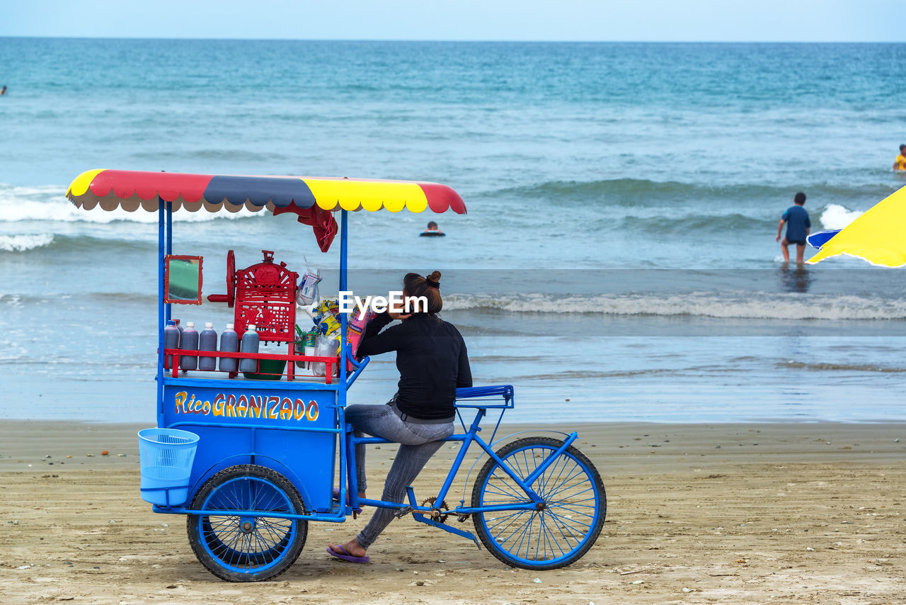 REAR VIEW OF MAN RELAXING ON BEACH