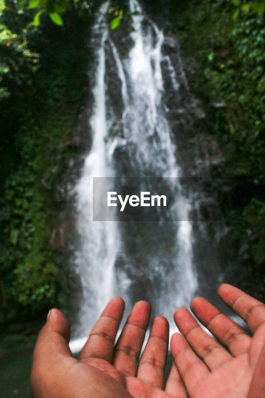 Cropped image of person hand on waterfall