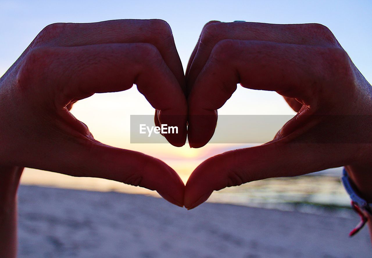 CLOSE-UP OF HANDS HEART SHAPE AGAINST SKY