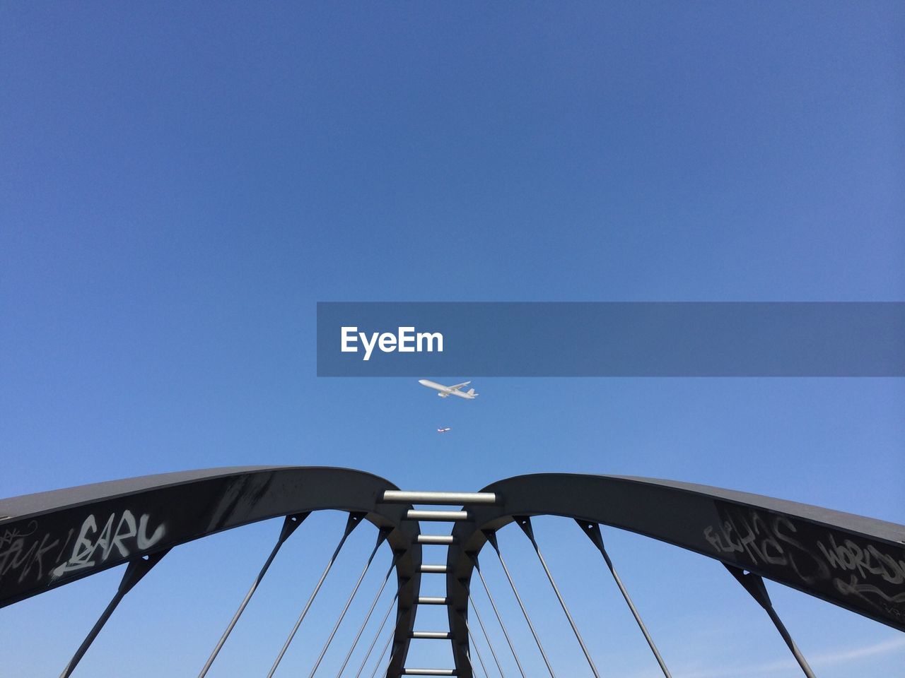 Low angle view of arch bridge against airplane in clear blue sky