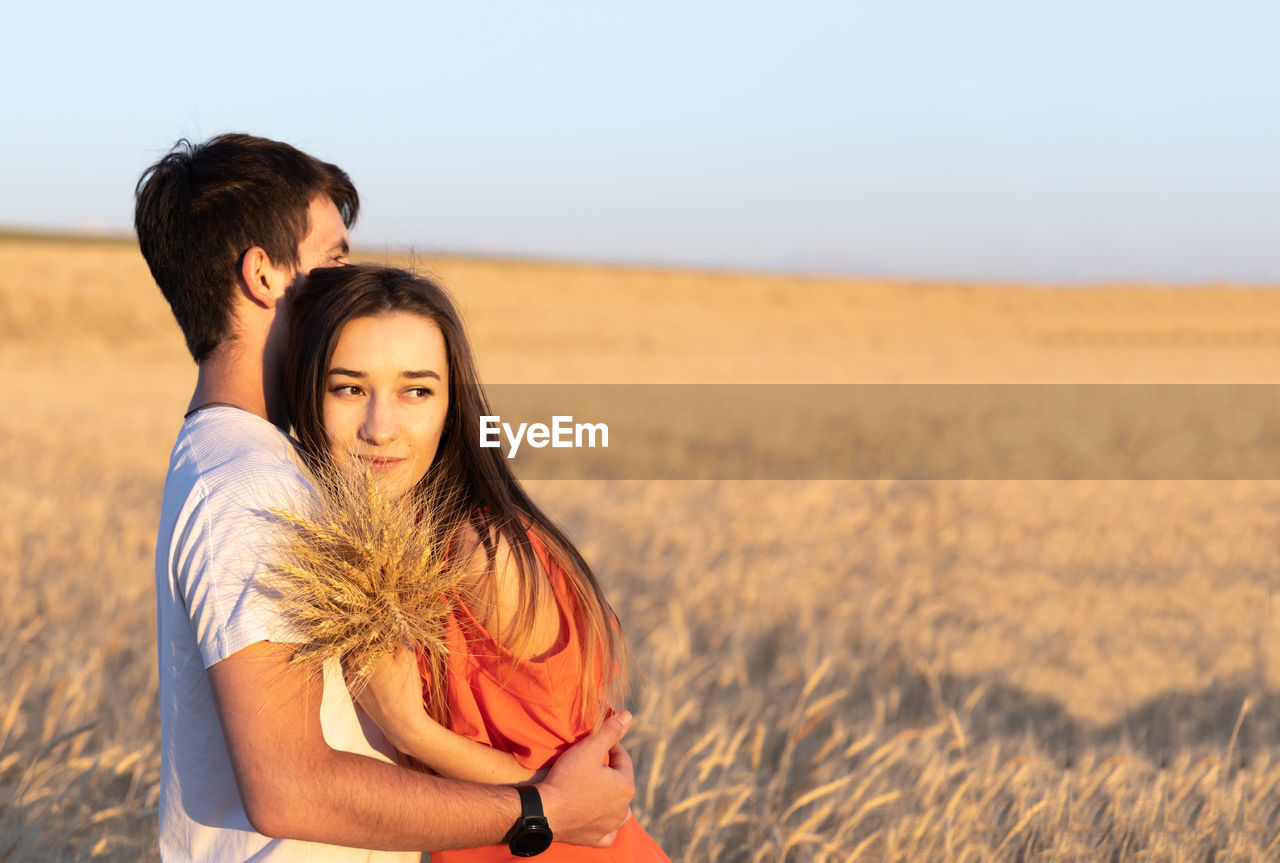 Young man hugging his girlfriend on sunset in wheat field. copy space, love, togetherness concept.