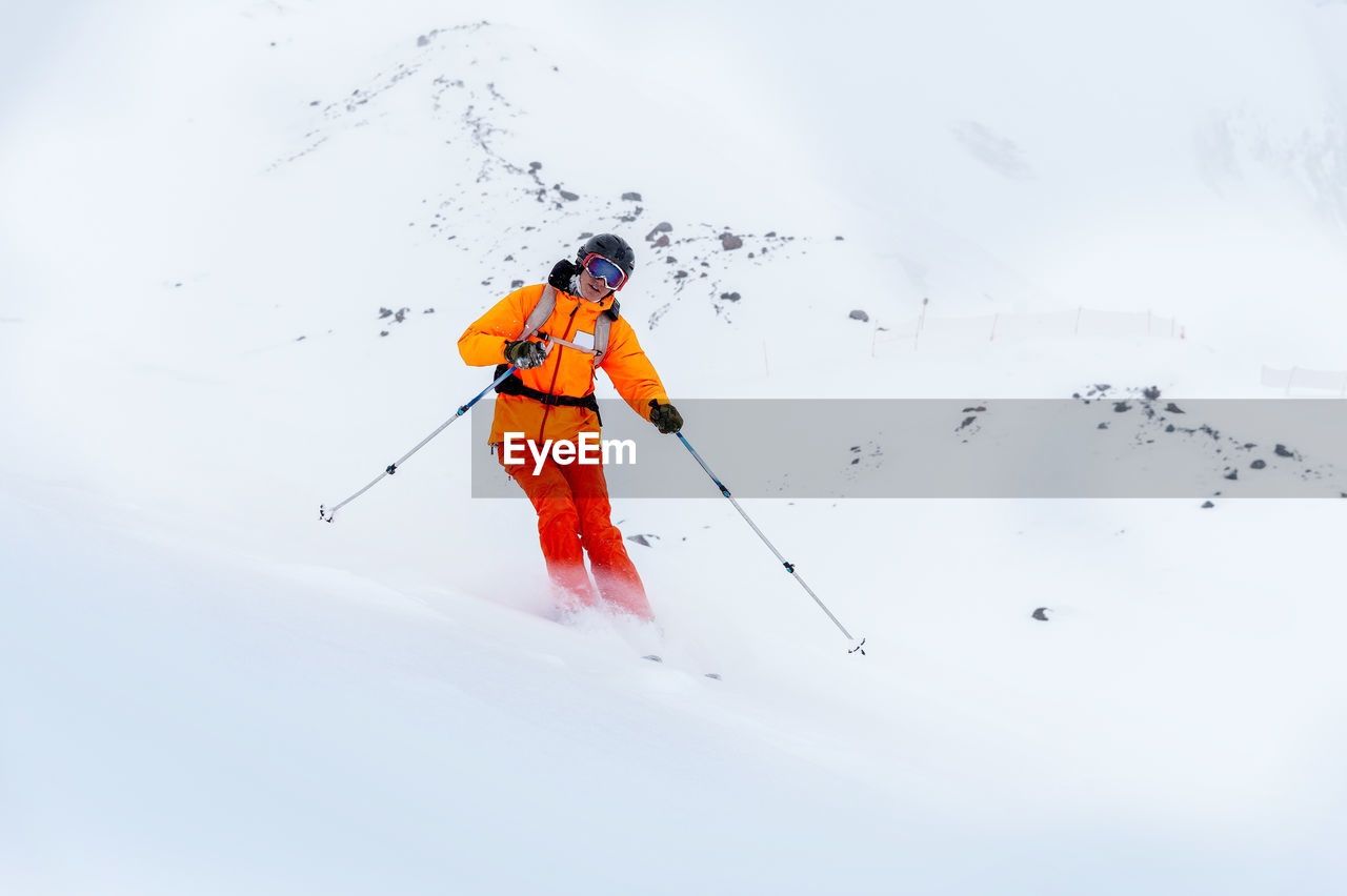 A young male skier in an orange ski suit rides a snowy mountainside in poor visibility. 