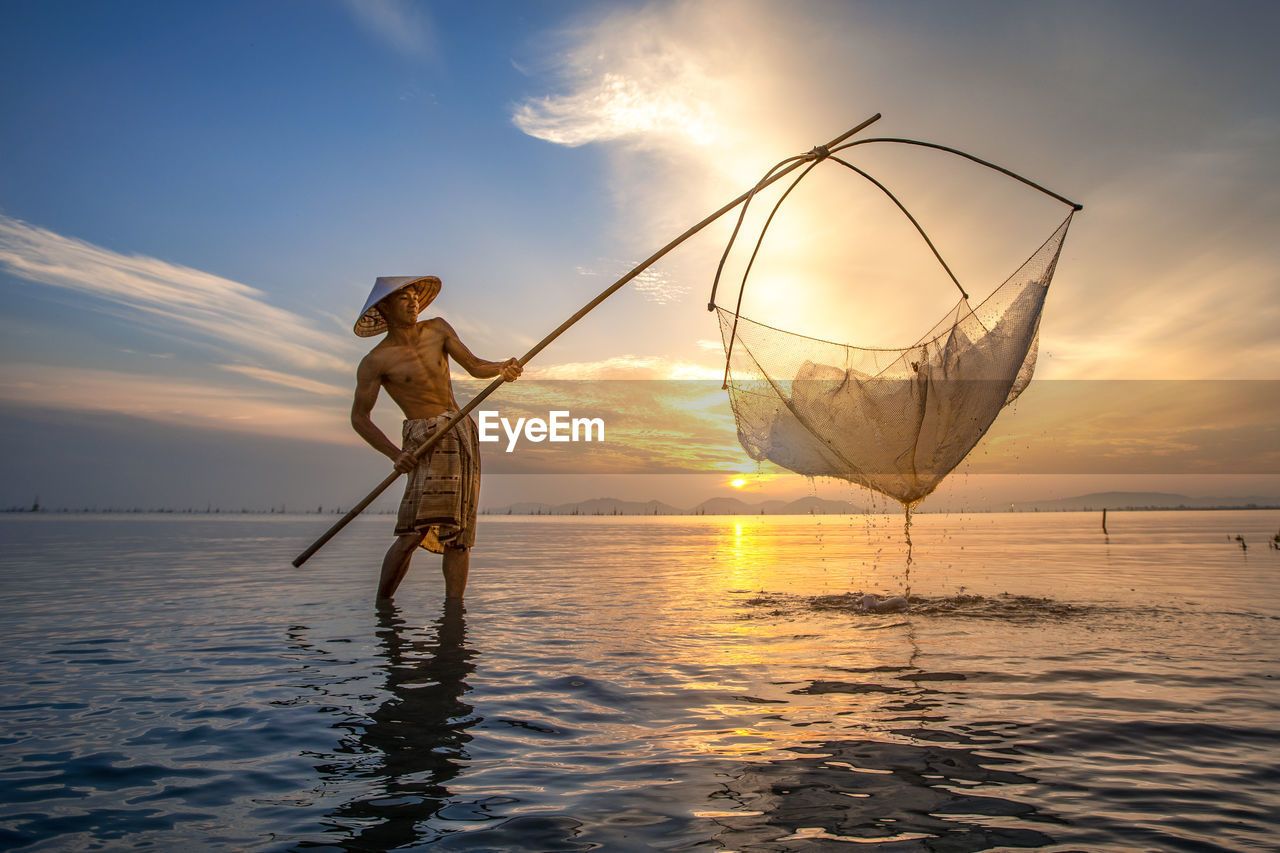 MAN FISHING IN SEA AGAINST ORANGE SKY