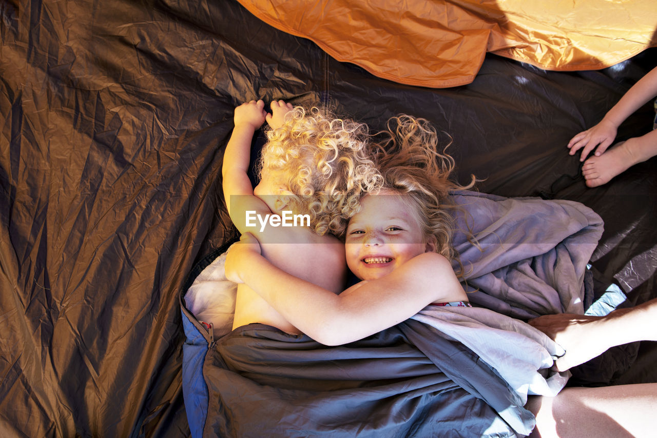 High angle view of siblings resting in sleeping bag at tent