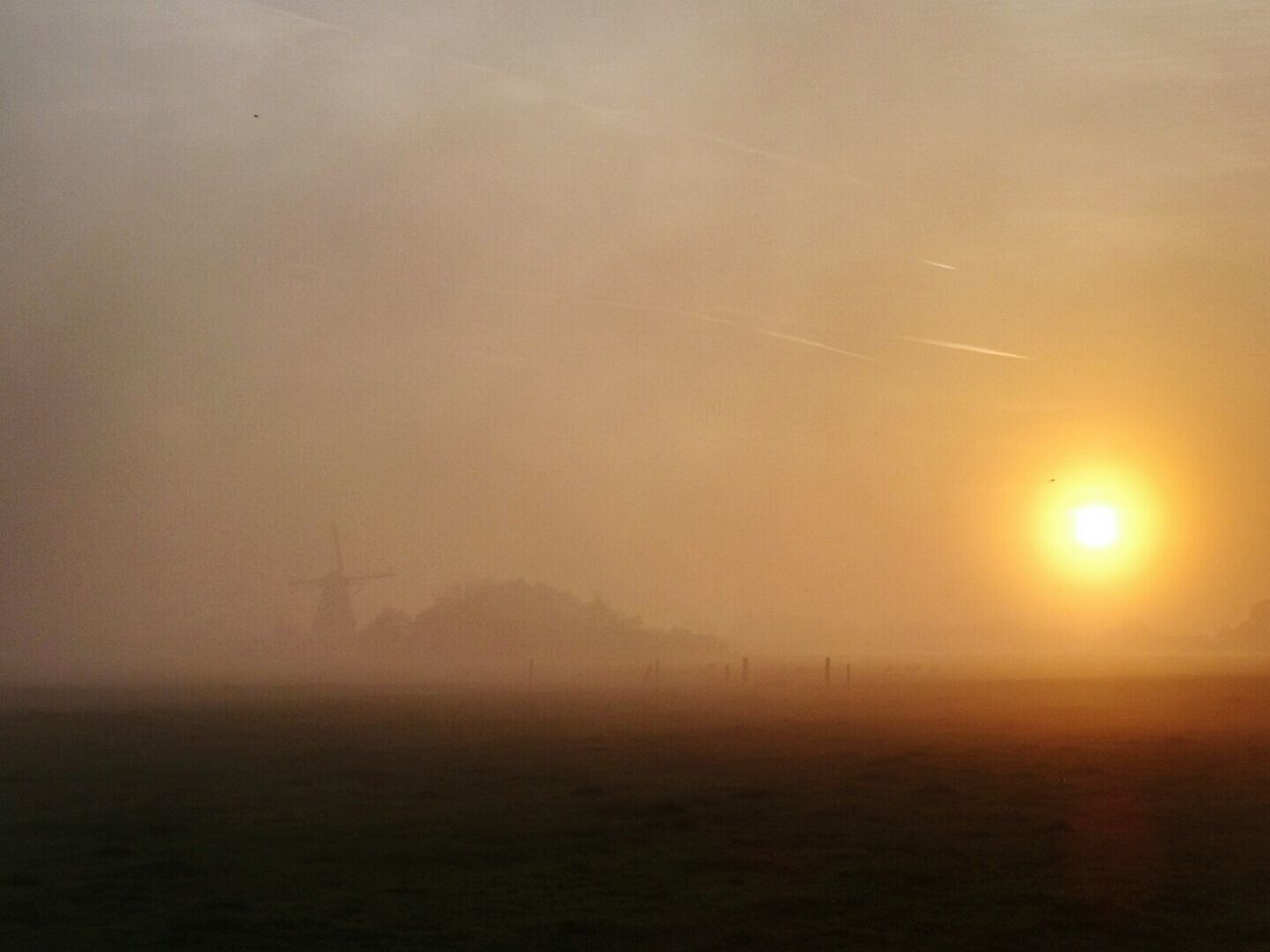 Scenic view of sunset over landscape during foggy weather