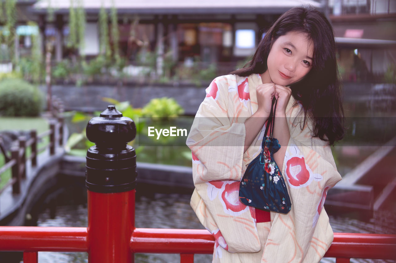 PORTRAIT OF BEAUTIFUL YOUNG WOMAN STANDING BY RAILING