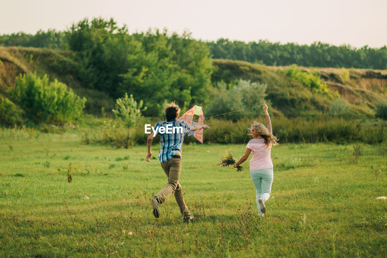 Couple flying kite on field against sky