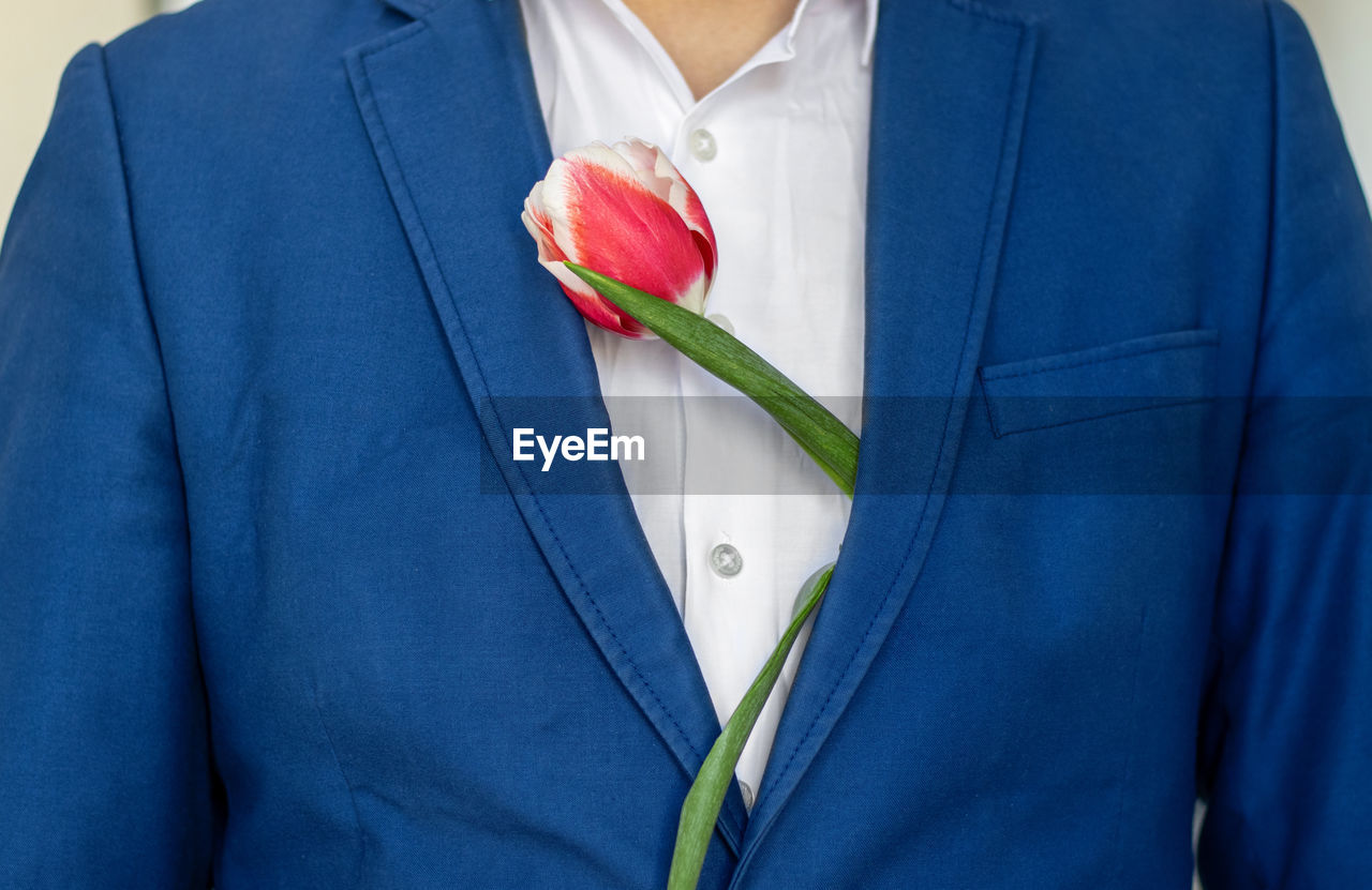 flower, blue, adult, midsection, one person, formal wear, close-up, tuxedo, clothing, men, indoors, love, emotion, studio shot, flowering plant, positive emotion, front view, business, blazer, plant, holding, outerwear, menswear, necktie, red, button down shirt, rose, sleeve