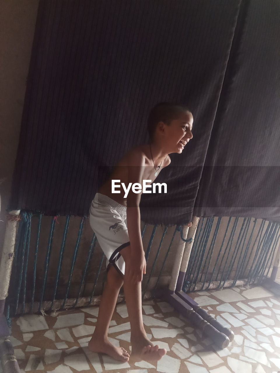 SIDE VIEW OF SHIRTLESS BOY STANDING ON FLOOR AT HOME