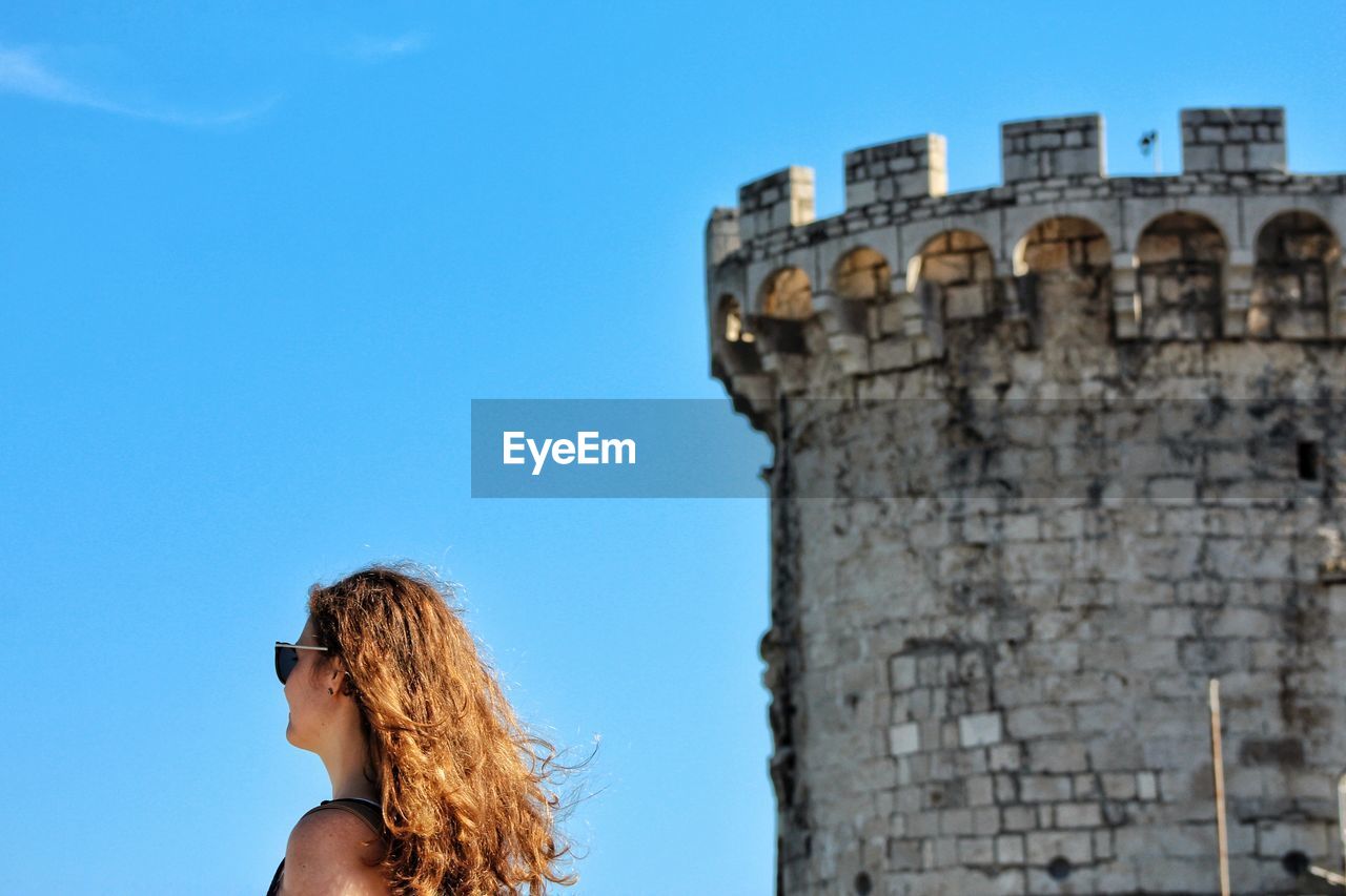 Low angle view of woman with castle in background against blue sky