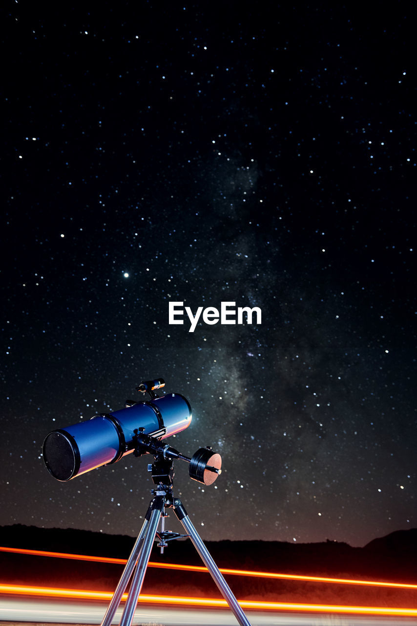 Modern optical telescope against cloudless dark sky with glowing stars at night time