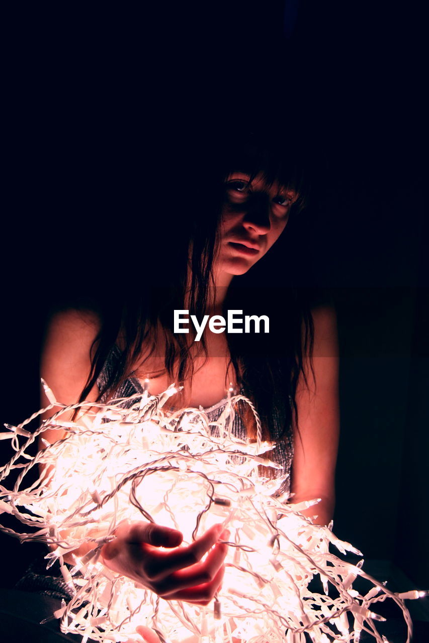 Teenage girl with illuminated fairy lights in darkroom at home