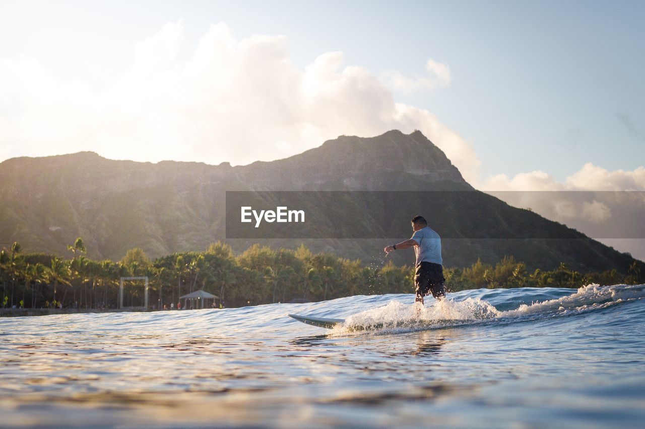 MAN STANDING IN SEA AGAINST MOUNTAINS