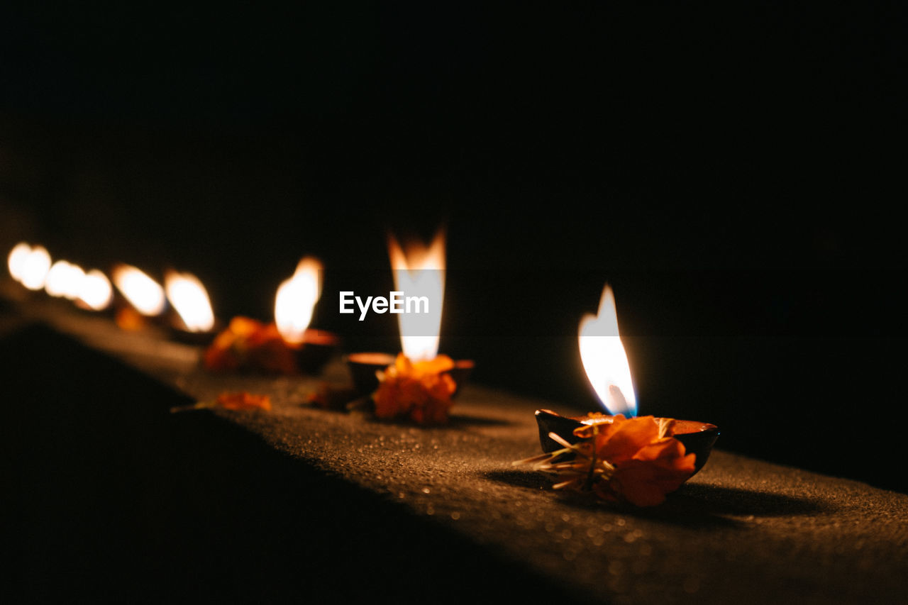 Close-up of diyas with flowers on retaining wall at night