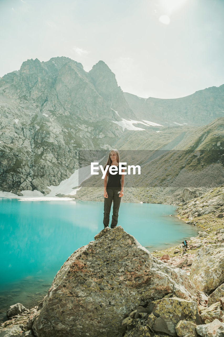 MAN STANDING ON ROCK LOOKING AT MOUNTAINS