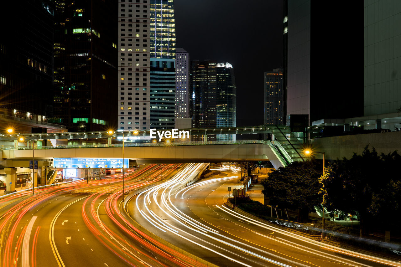 Light trails on road by illuminated buildings in city at night