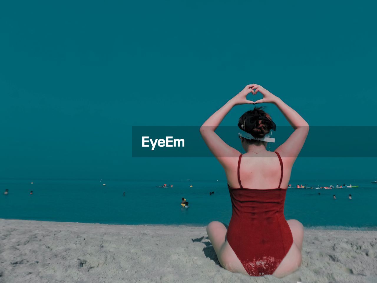 Rear view of woman making heart shape at beach against clear blue sky