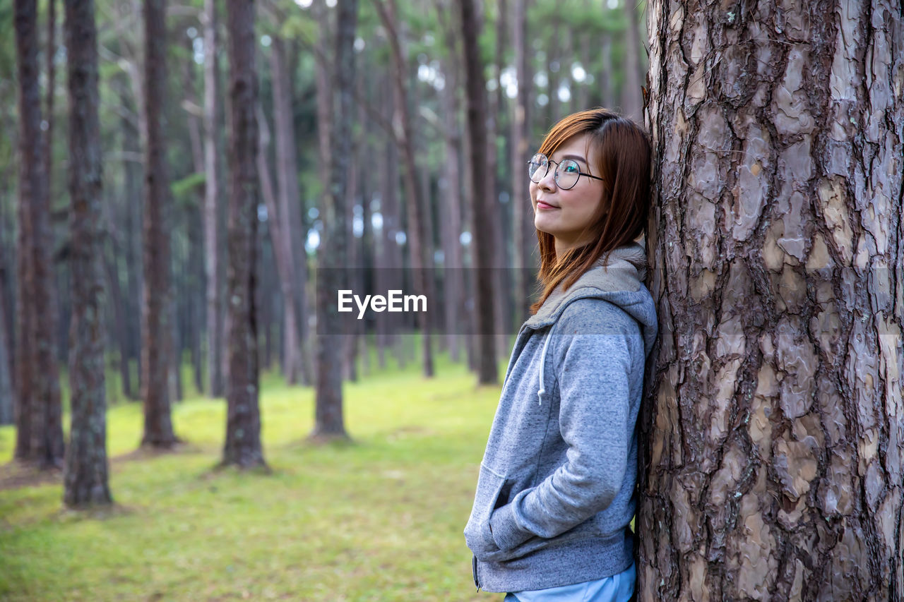 Side view of woman standing by tree trunk in forest