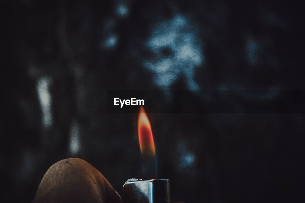 Close-up of human hand holding burning cigarette lighter at dusk