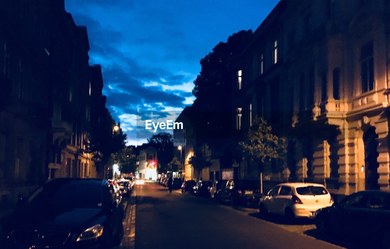 CARS ON ROAD AMIDST BUILDINGS AT DUSK