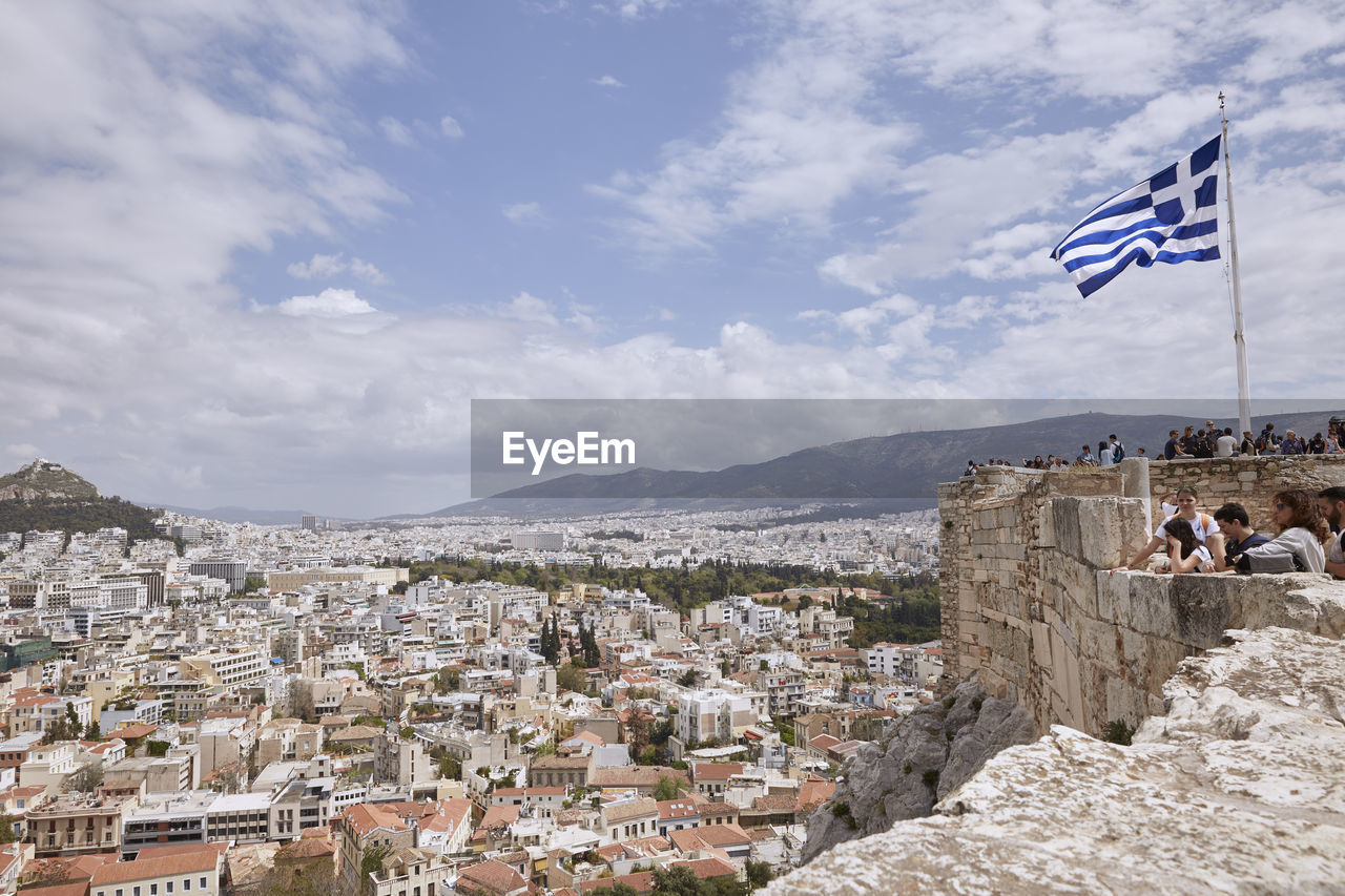 People with greek flag at acropolis of athens looking at townscape against sky