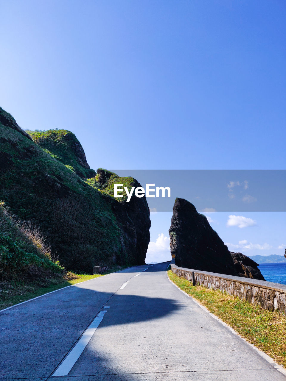 Empty road by mountain against clear blue sky