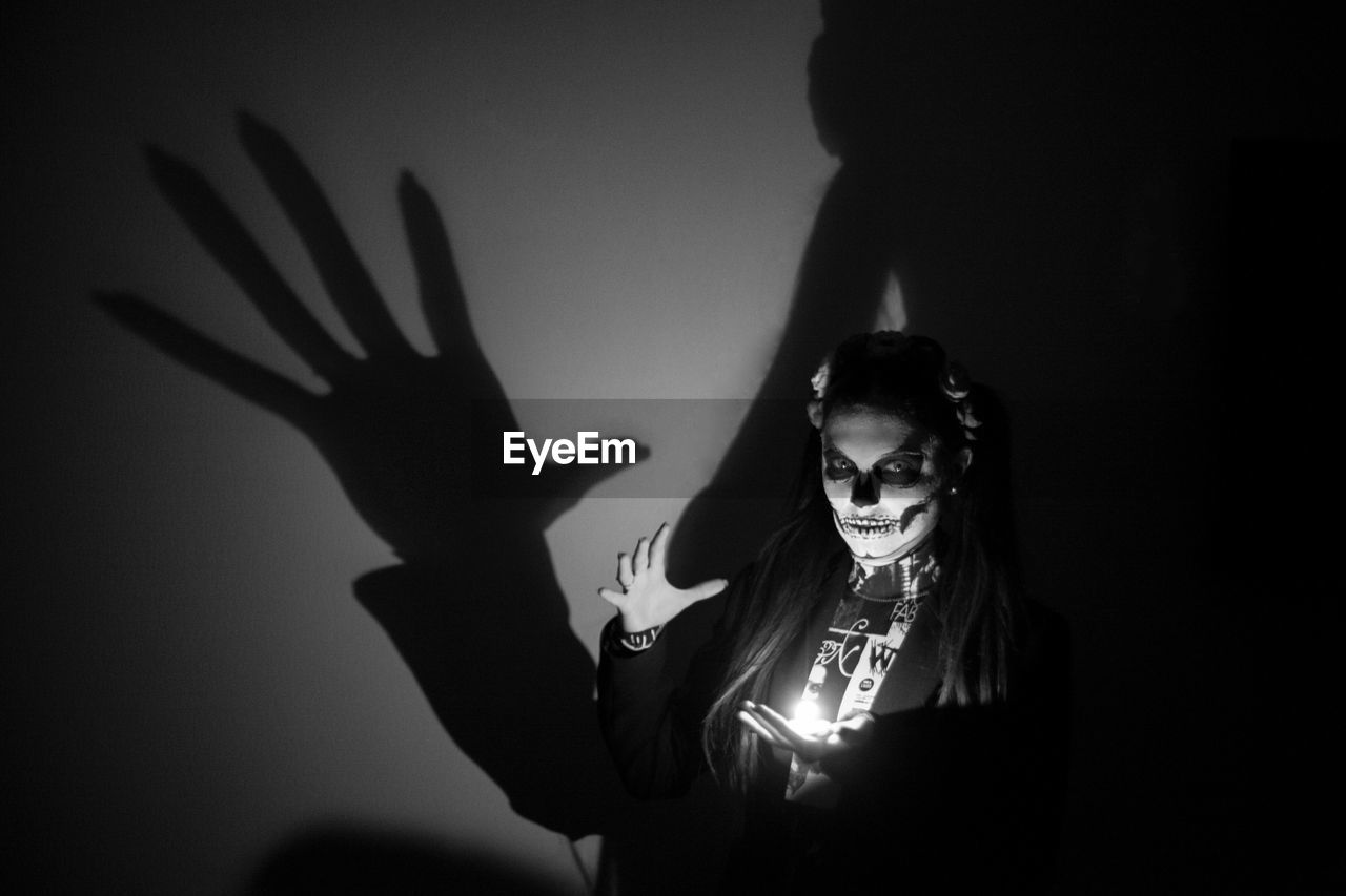 Portrait of spooky woman standing with illuminated lighting equipment in darkroom