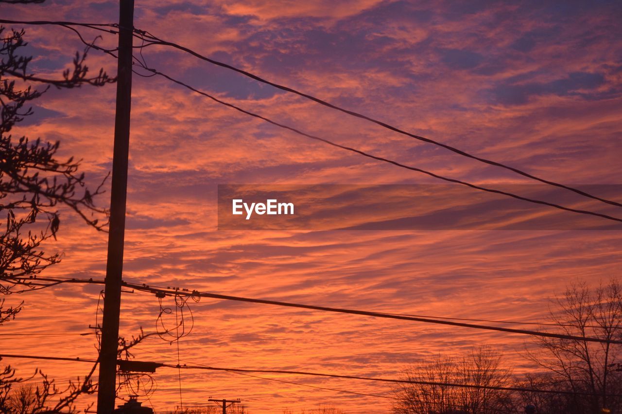 Silhouette electricity pylon against dramatic sky during sunset