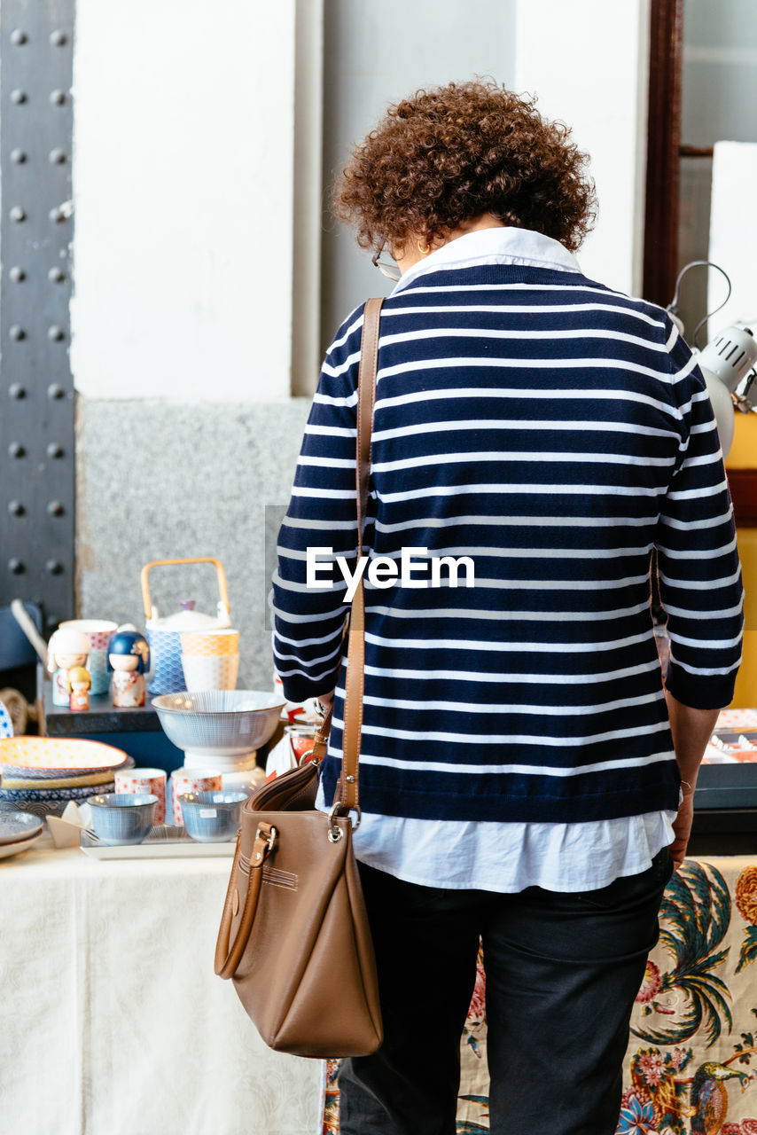 rear view, one person, clothing, adult, striped, indoors, casual clothing, standing, curly hair, women, three quarter length, lifestyles, hairstyle, business, sleeve, bag, young adult, day, business finance and industry, window, person, holding, pattern, handbag, leisure activity, spring, food and drink, domestic life, retail, fashion