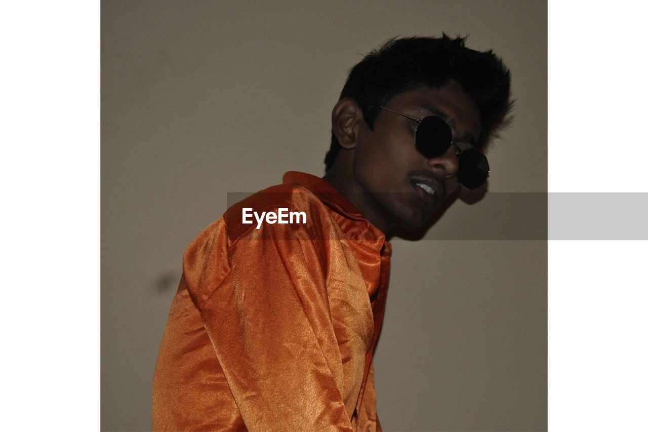 Young man wearing sunglasses against wall at home