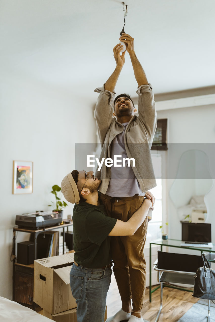 Side view of man embracing boyfriend installing bulb at home