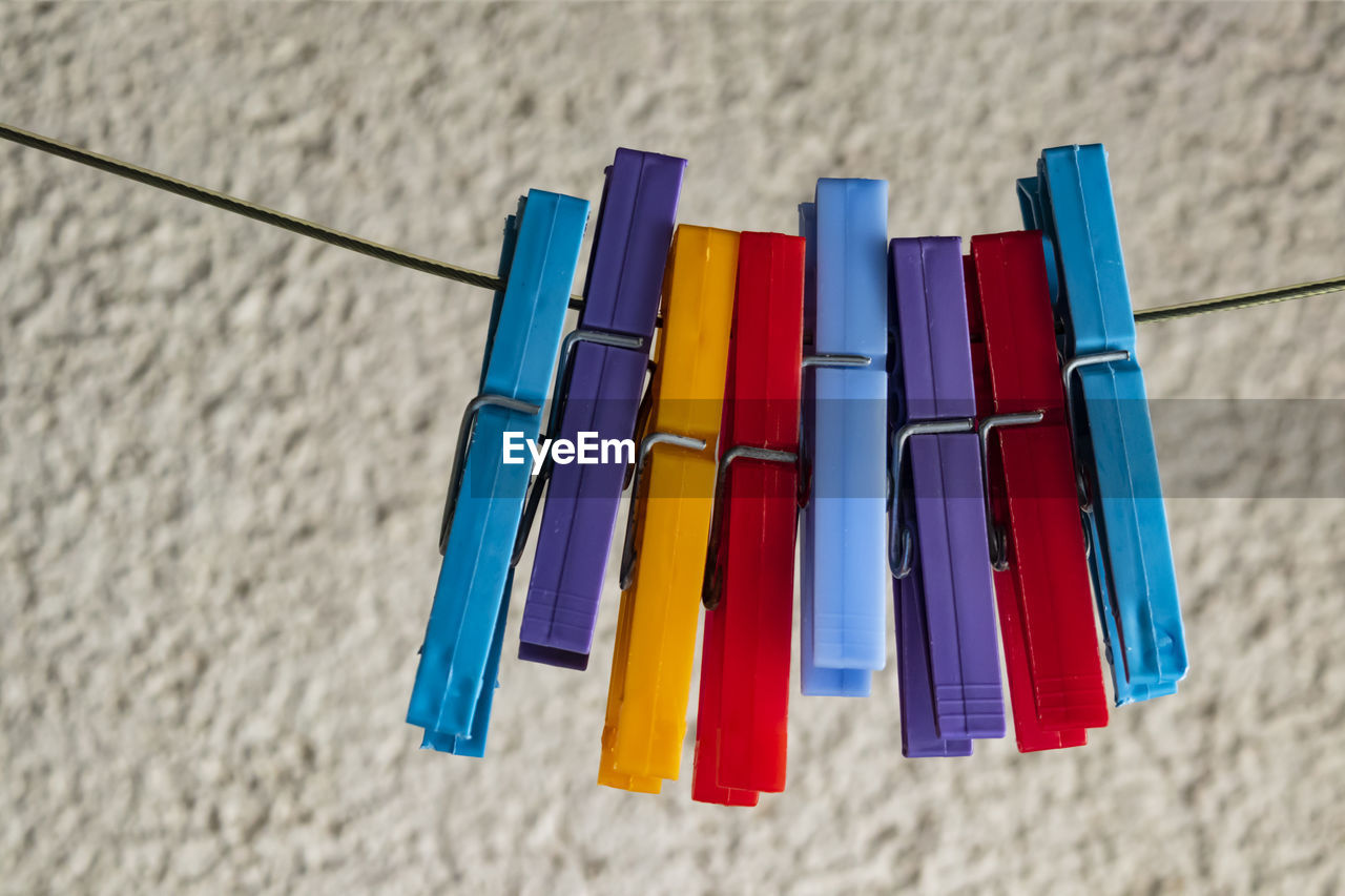 Close-up of multi colored clothespins on clothesline against wall