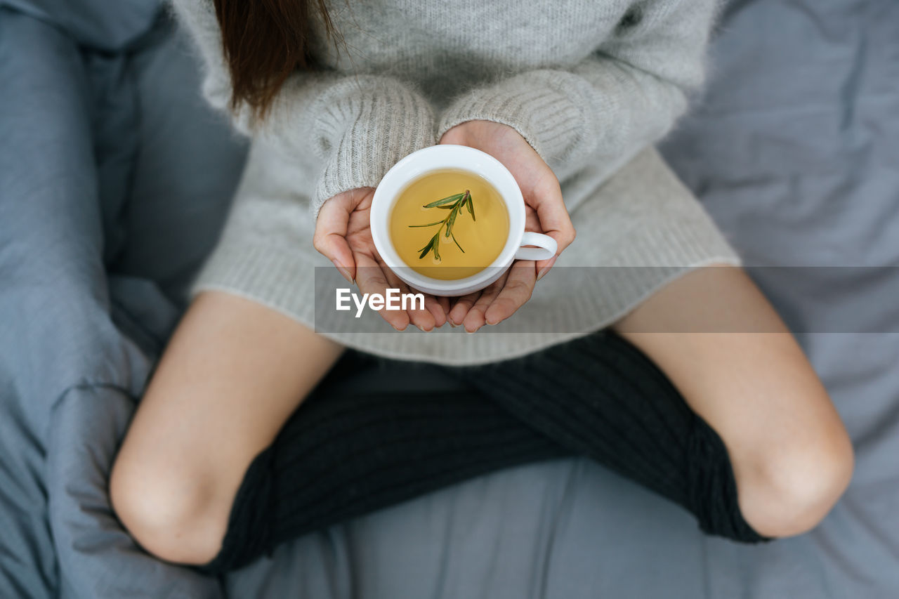 midsection of woman holding alarm clock on sofa at home