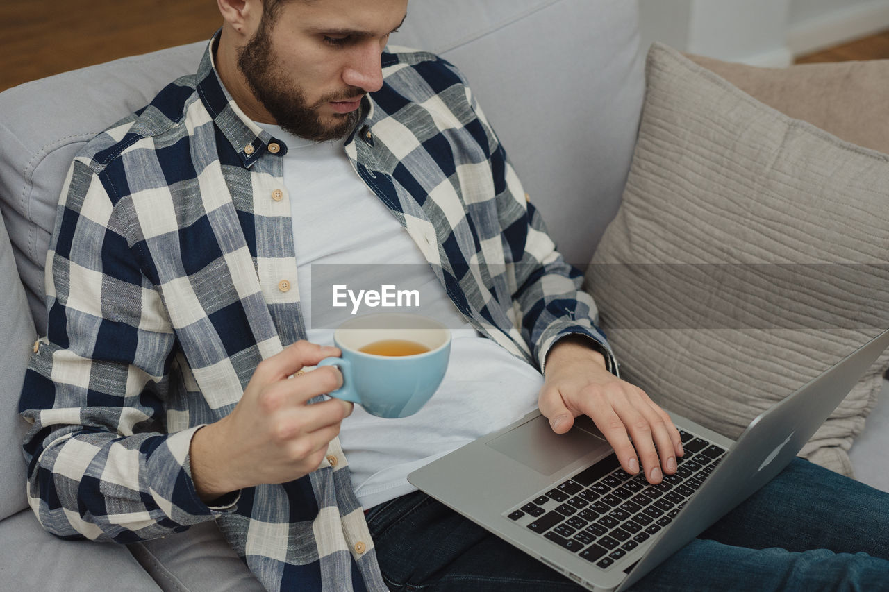 man using laptop while sitting on sofa at home