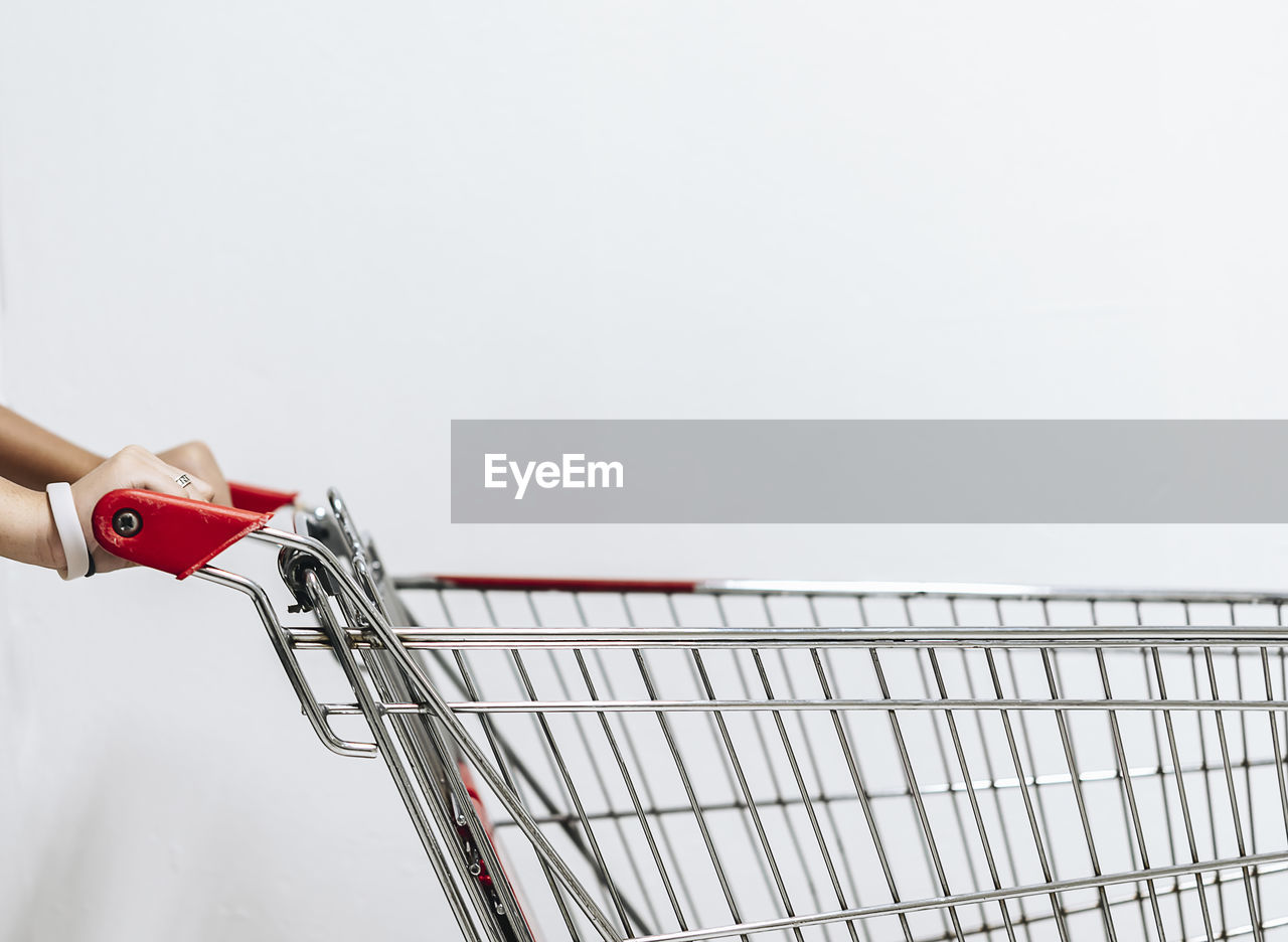 Cropped hands of woman holding shopping cart against white background