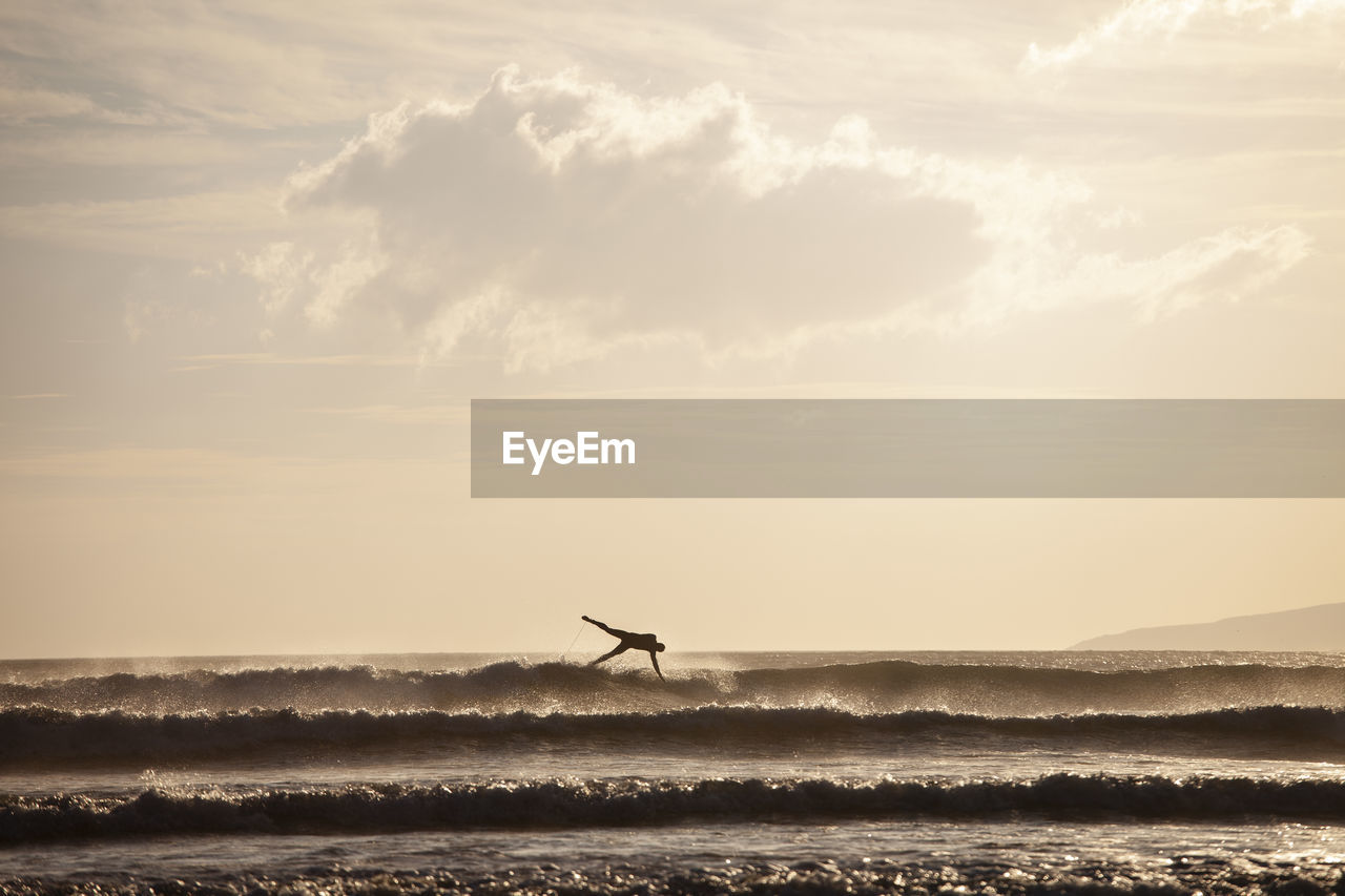 Silhouette man falling while surfing in sea against sky during sunset