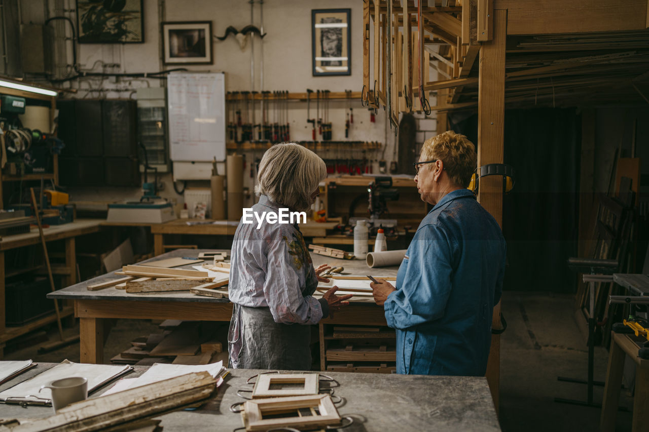 Senior craftswomen discussing together while working at repair shop