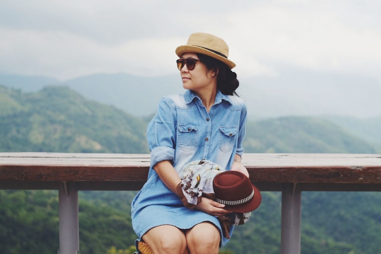 Young woman wearing sunglasses and hat at observation point against mountains