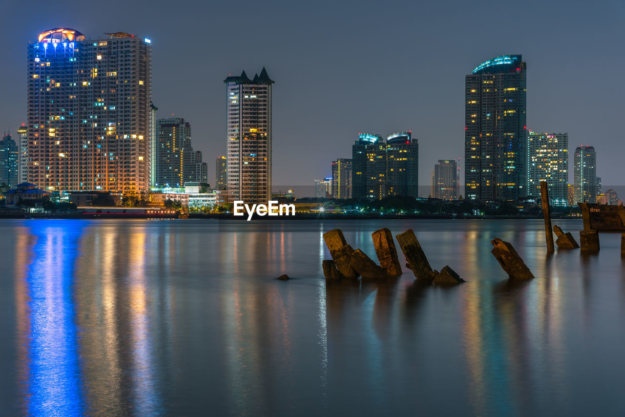Illuminated buildings by chao phraya river against sky