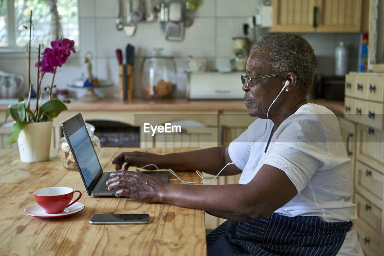 Senior woman sitting at kitchen table using laptop