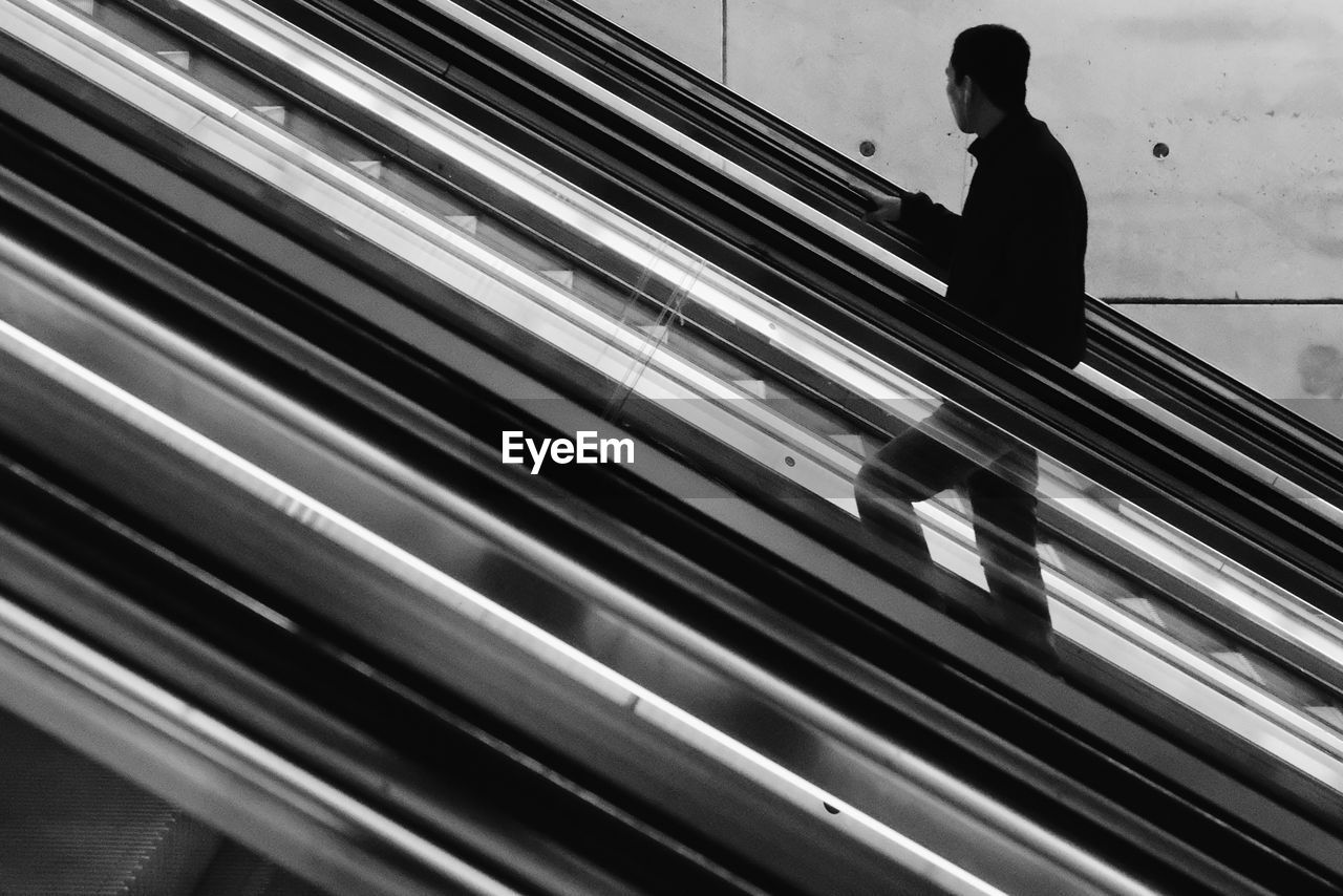 REAR VIEW OF MAN LOOKING THROUGH WINDOW ON ESCALATOR